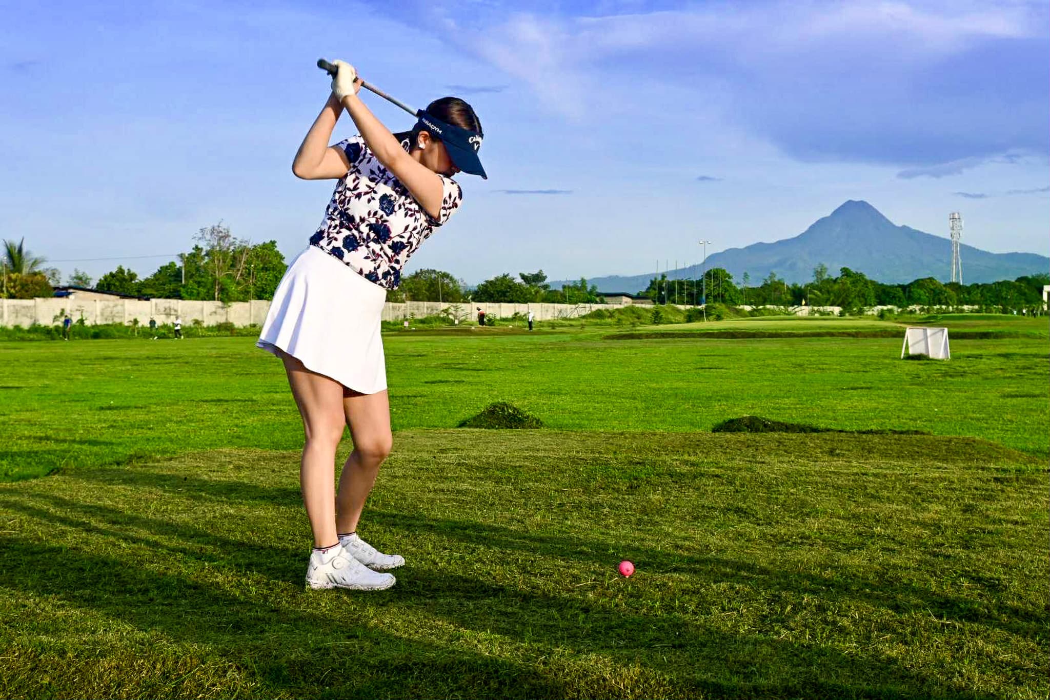A woman takes a graceful swing at Brigada Golf Range in General Santos City, with the stunning silhouette of Mt. Matutum framing the horizon.